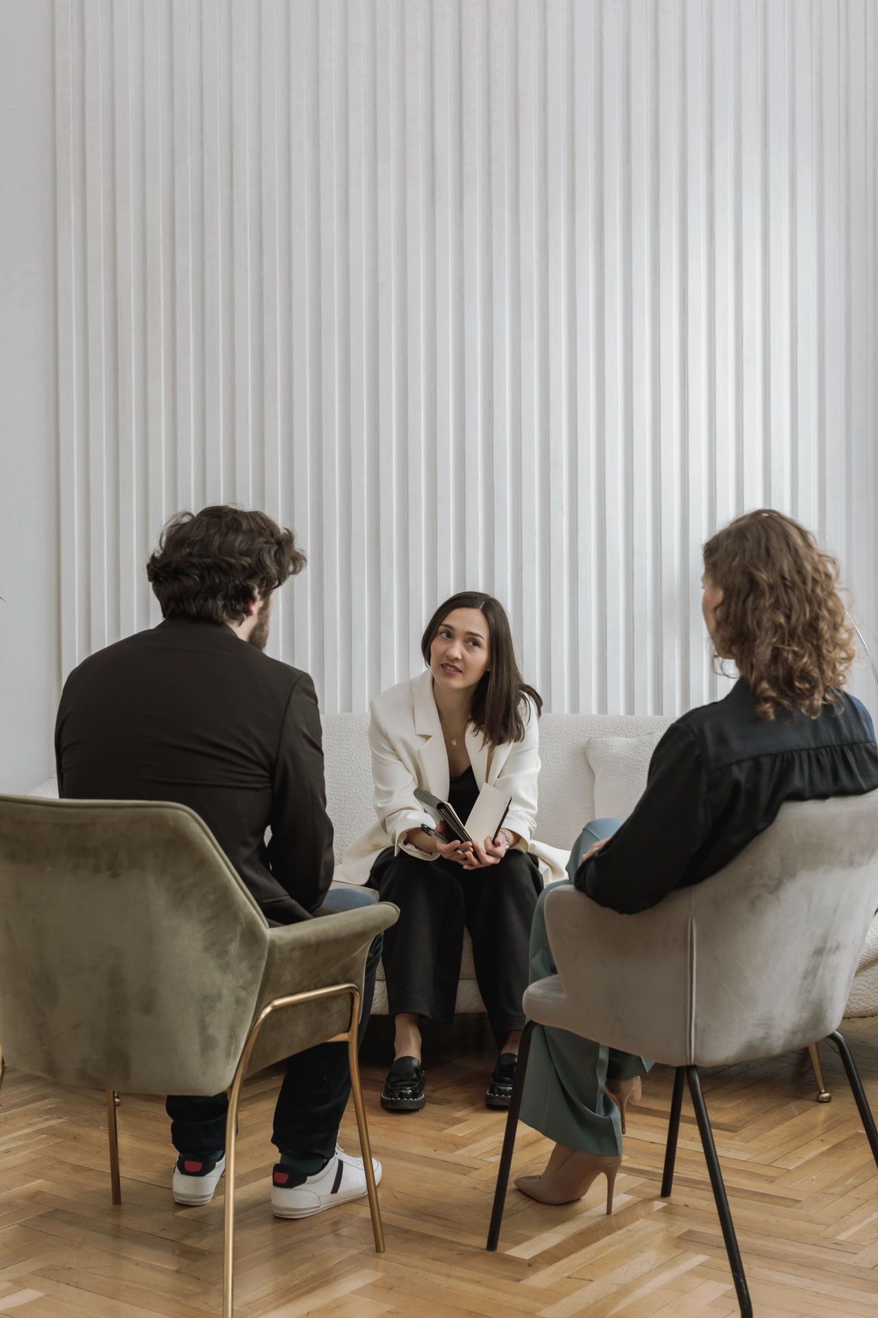 Drei Personen in einem Gespräch, in einem modernen Raum mit Holzboden und weißen Wänden.