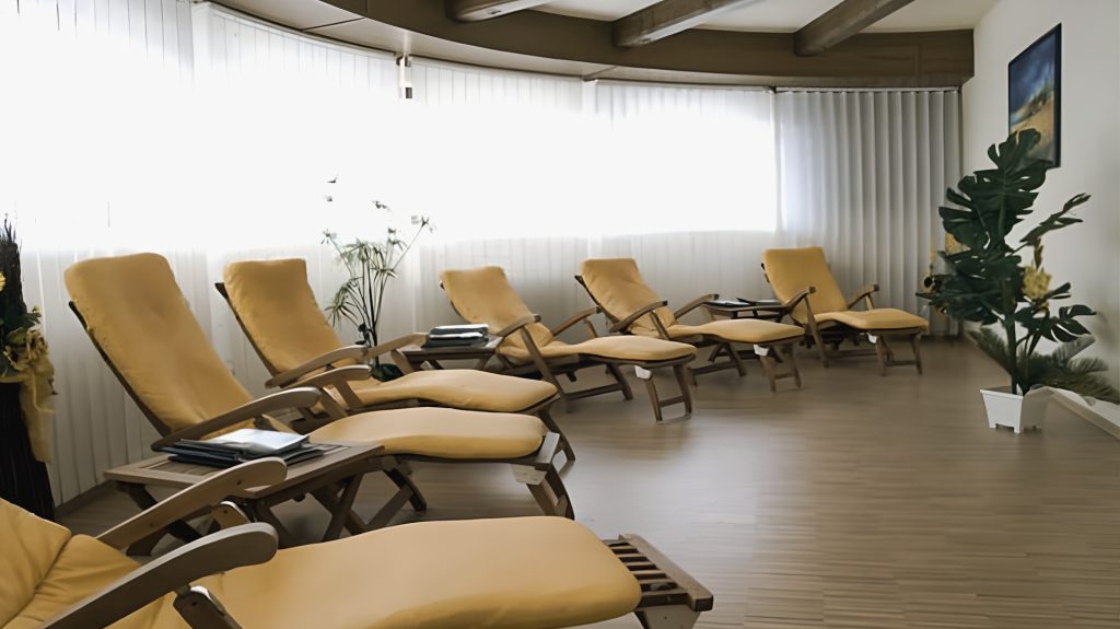 Heller Ruheraum mit sechs gelben Liegestühlen, Pflanzen und Holzboden.