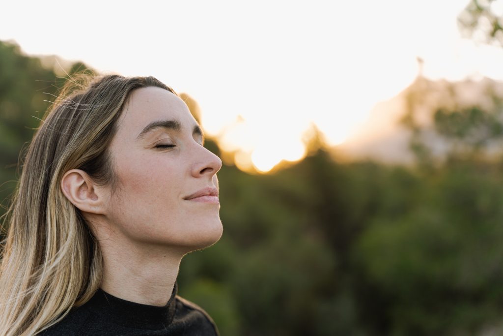 Frau mit geschlossenen Augen genießt die Natur bei Sonnenuntergang.